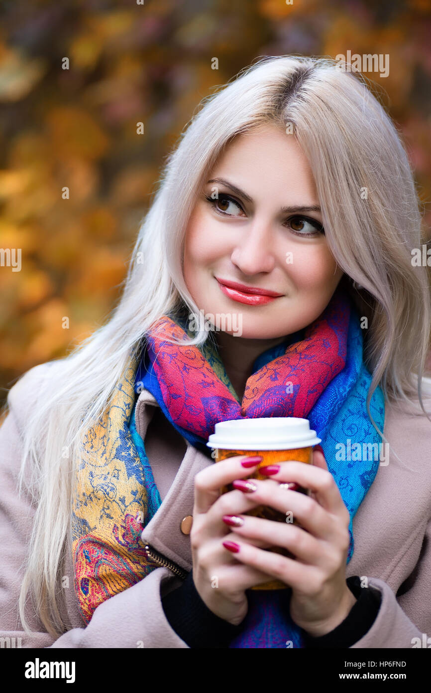 Jeune fille blonde à emporter de maintien de verre dans les mains. À l'extérieur. Fille avec tasse de café dans le parc de l'automne. Concept d'automne - automne woman drinking coffee in park Banque D'Images