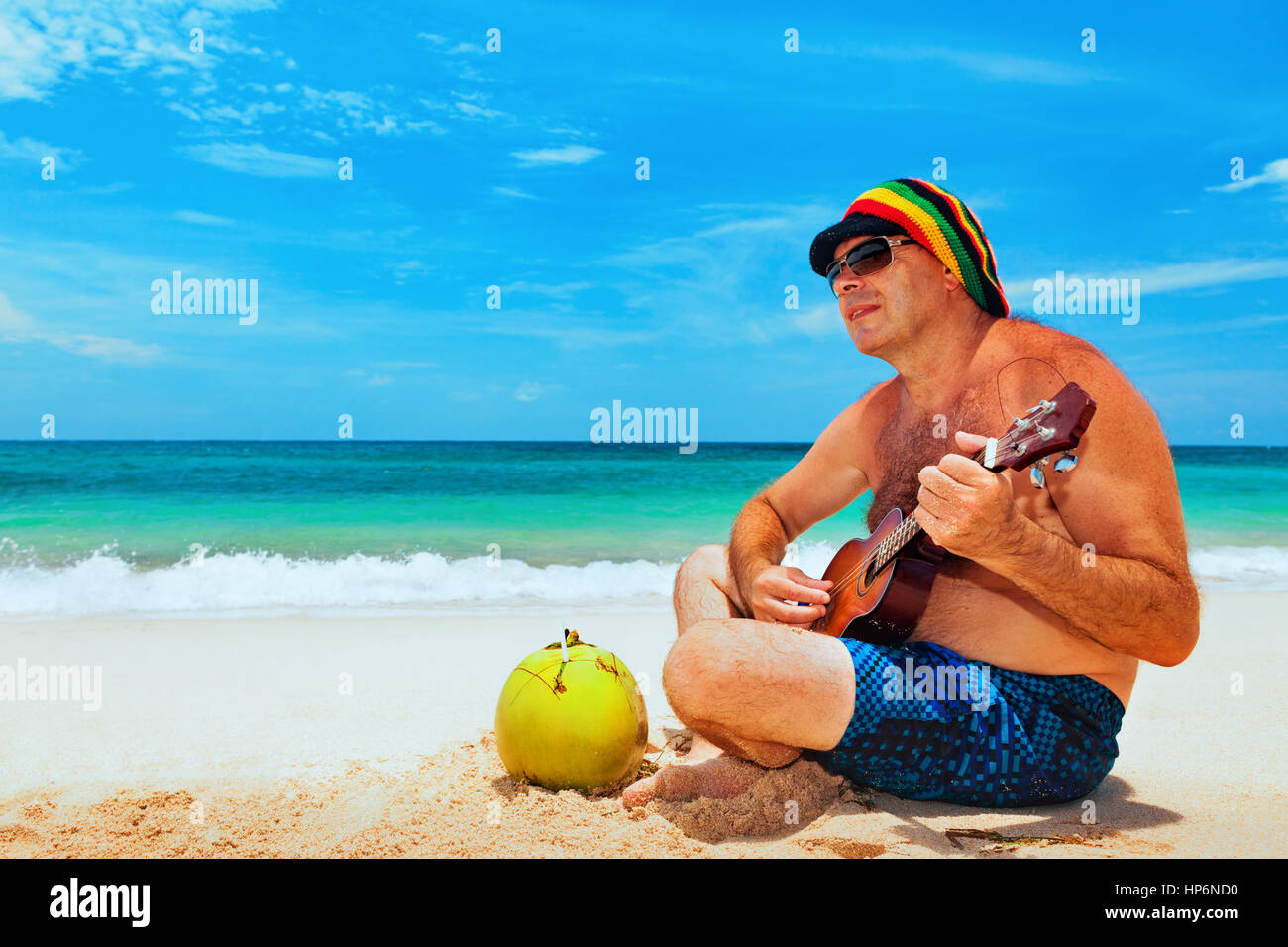 Heureux l'homme à l'âge de retraite chapeau a l'amusement, jouer la musique reggae sur guitare hawaïenne, profiter caribbean beach party. Mode de vie des aînés et les loisirs. Banque D'Images