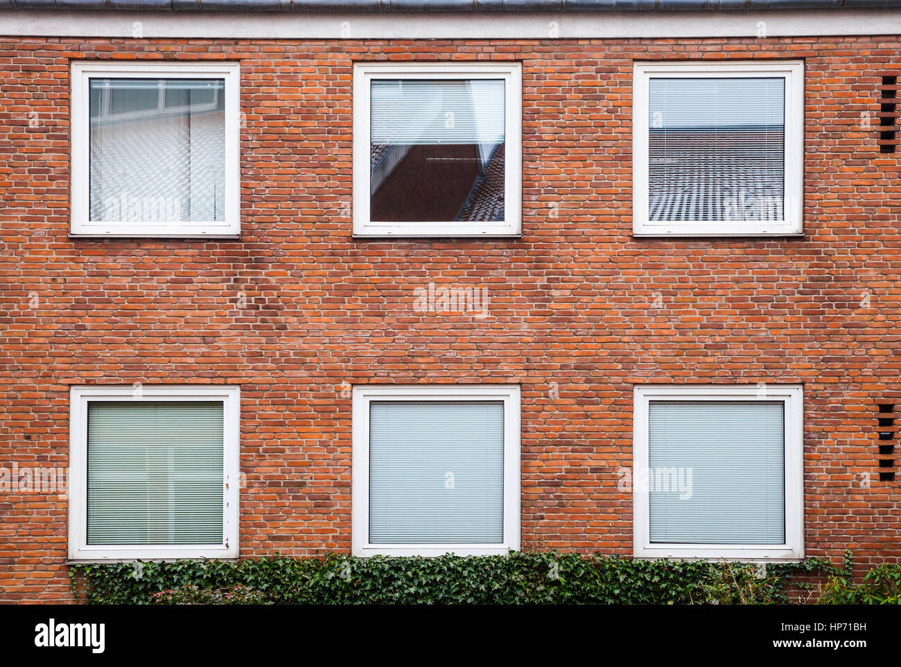 Mur de briques rouges avec des fenêtres carrées fermé avec persiennes blanc, façade de maison de vie européen, la texture d'arrière-plan Banque D'Images