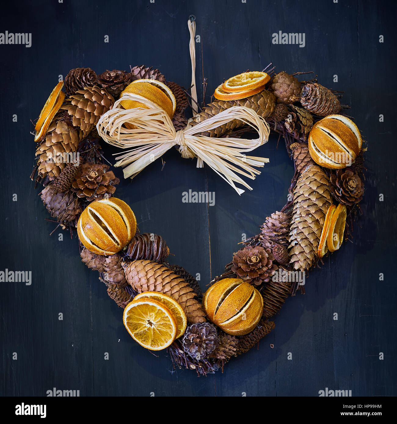 Couronne de coeur de Noël fabriqués à partir de pommes de pin et des oranges séchées sur un fond de bois Banque D'Images