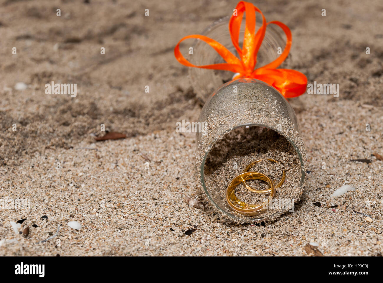 Deux anneau de mariage à l'intérieur d'une vitre avec un ruban orange sur le sable Banque D'Images