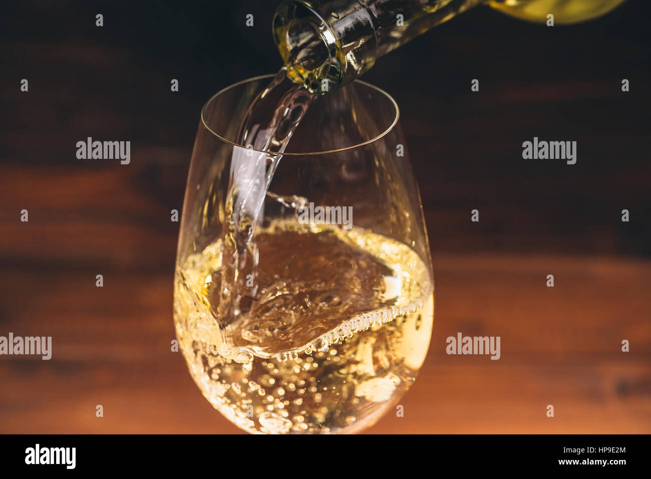 Verser le vin blanc à partir d'une bouteille dans une vue rapprochée de l'wineglasses contre fond de bois Banque D'Images