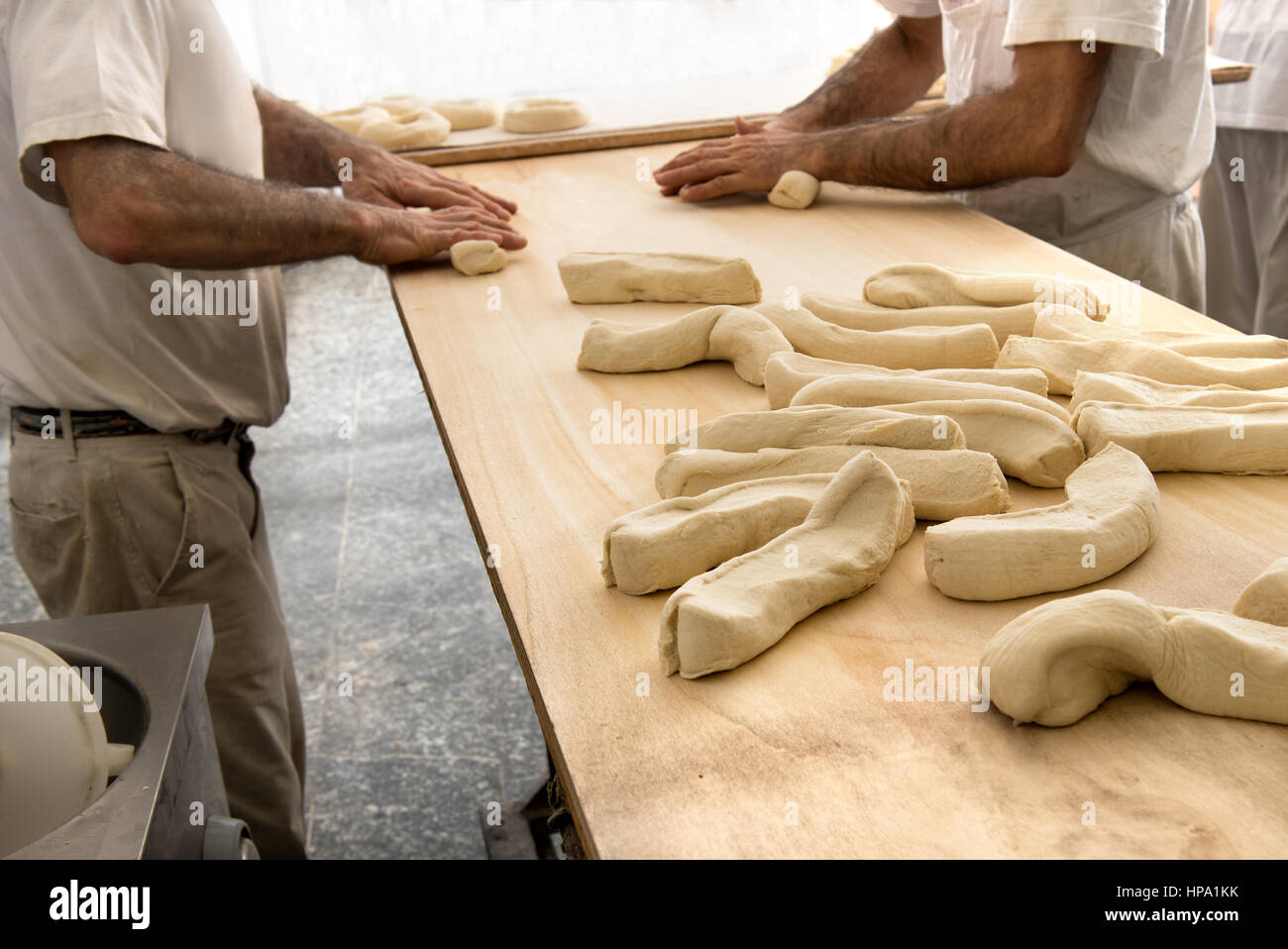 Deux boulangers mâle incognito la pâte de roulement avec les mains faire le pain, se tenant à table dans une boulangerie Banque D'Images