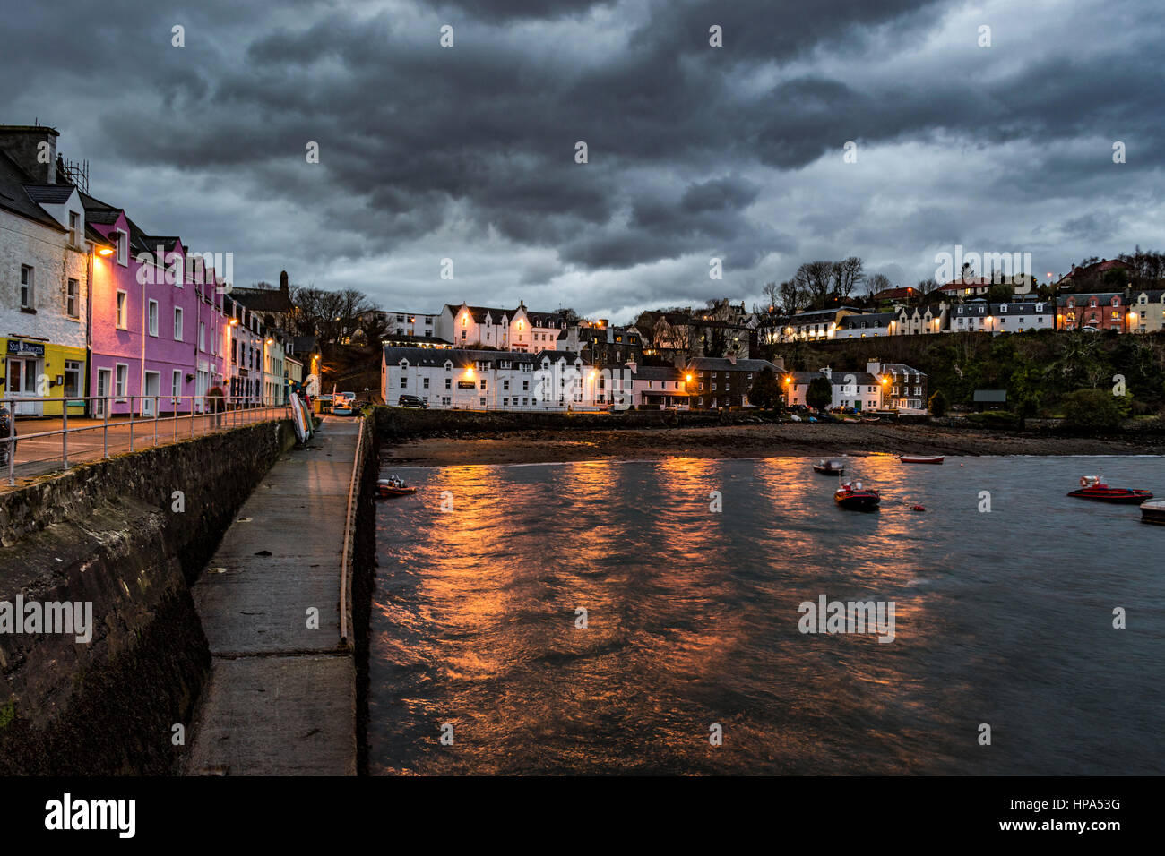 Le port de Portree, Isle of Skye, Scotland au crépuscule. Février 2017, montrant les bâtiments au crépuscule que les feux sont allumés, sur une sombre des nuages. Banque D'Images