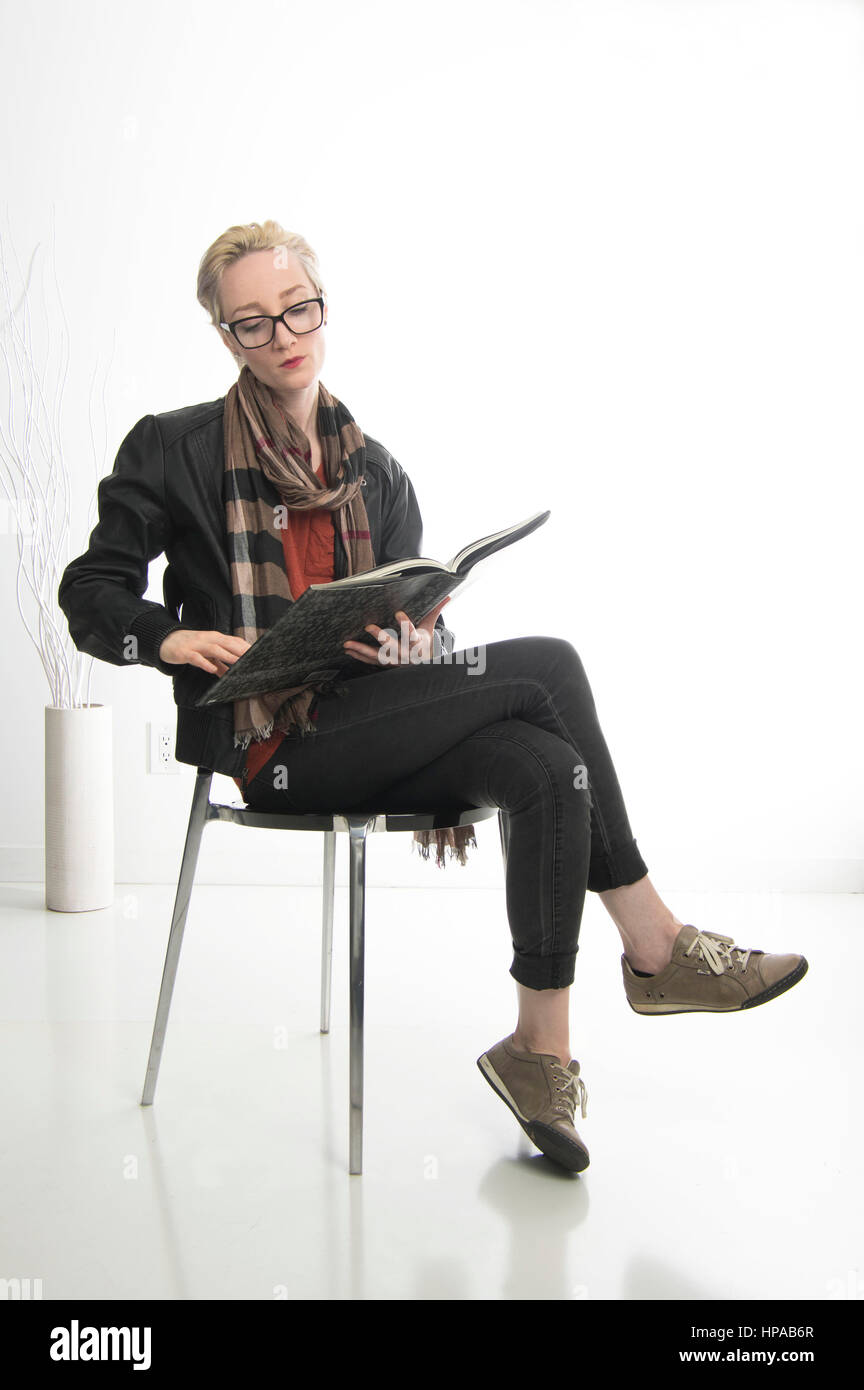 Femme blonde aux cheveux courts, portant des lunettes assis dans une salle de lecture d'un livre blanc Banque D'Images