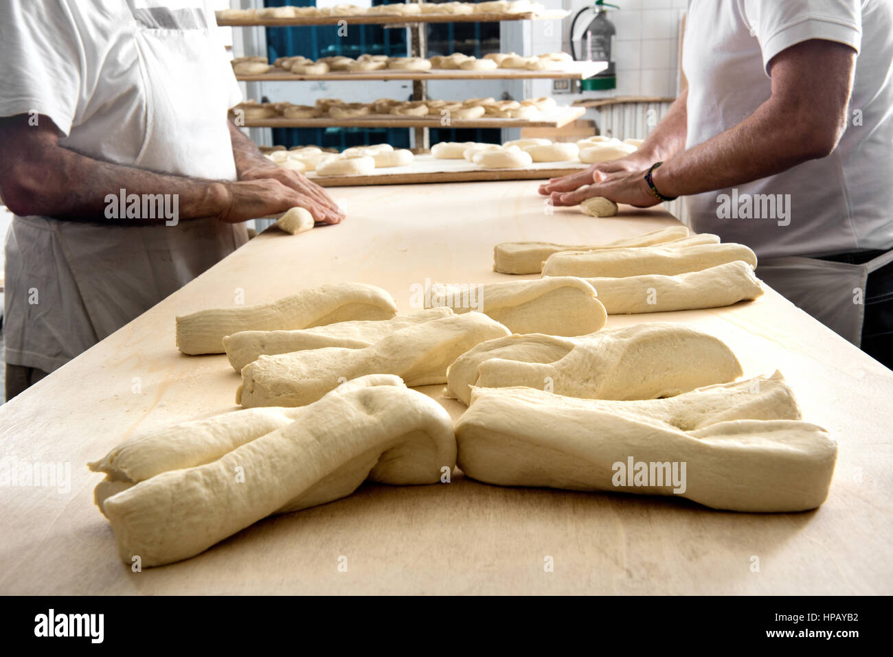 Deux boulangers mâle incognito la pâte de roulement debout les uns contre les autres à table en bois dans la boulangerie, les morceaux de pâte crue en premier plan Banque D'Images
