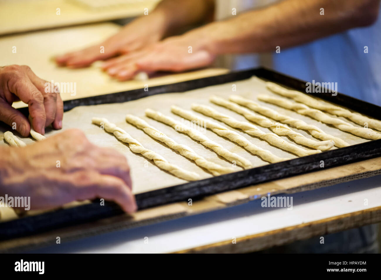 Travail manuel longuet, close-up de boulangers mâle mains tordant gressins pâte et la placer sur du papier sulfurisé dans le plateau métallique Banque D'Images