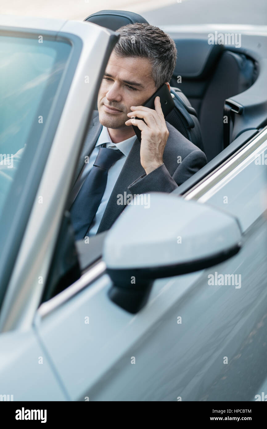 La conduite d'affaires une voiture décapotable de luxe et d'affaires ayant des appels téléphoniques à l'aide de son smartphone Banque D'Images