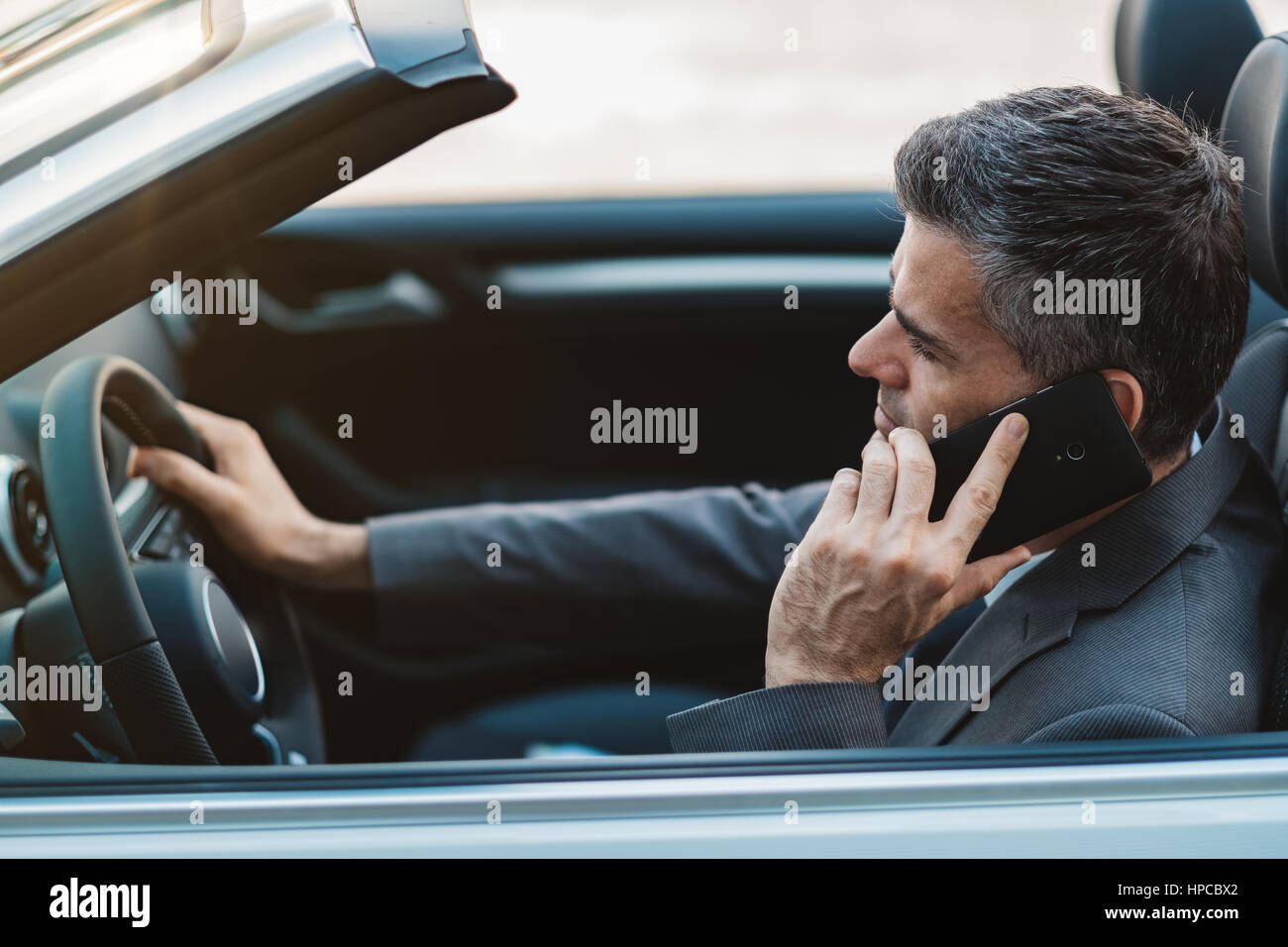 La conduite d'affaires une voiture décapotable de luxe et d'affaires ayant des appels téléphoniques à l'aide de son smartphone Banque D'Images