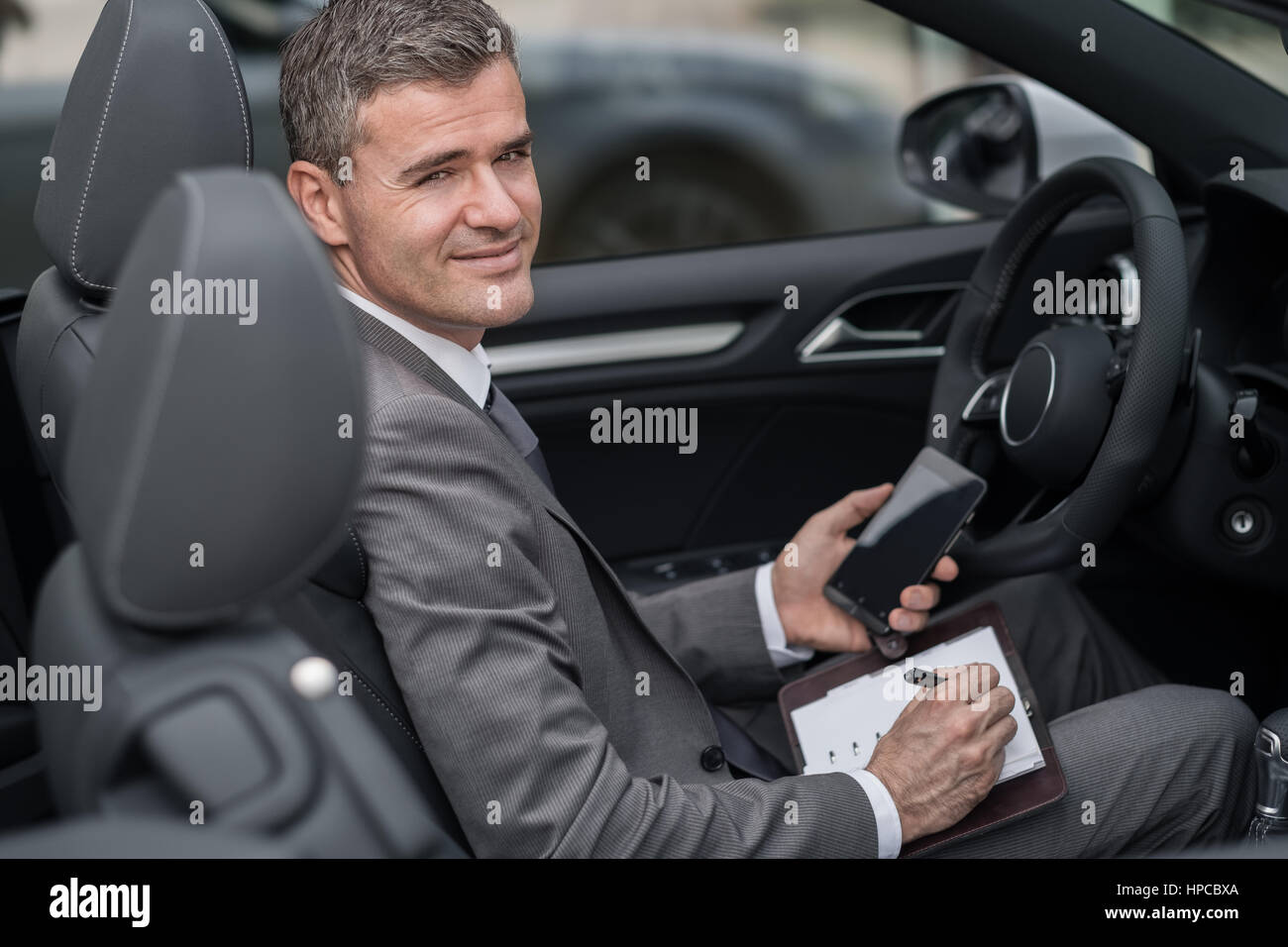 Portrait dans sa voiture, il est la planification et l'échéancier des réunions sur son organisateur et utiliser des applications sur son smartphone Banque D'Images