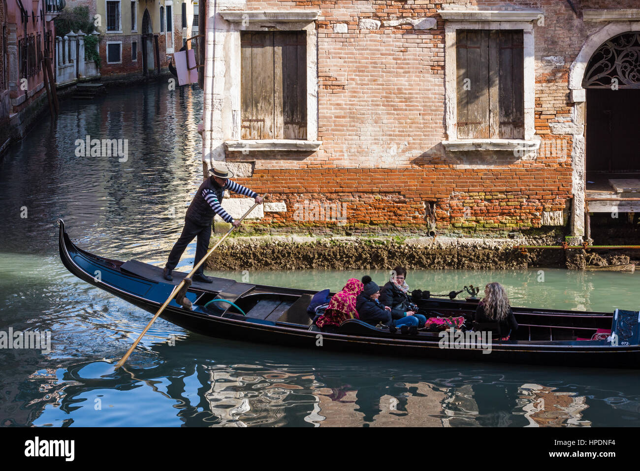 Un gondolier avec coiffe traditionnelle est considérée l'aviron le long d'un des canaux de Venise Italie Banque D'Images