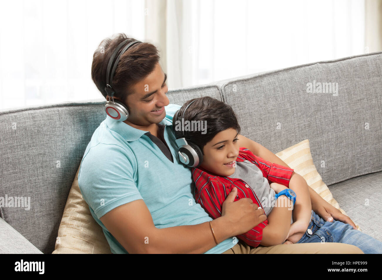 Père et fils d'écouter de la musique ensemble sur canapé avec un casque Banque D'Images