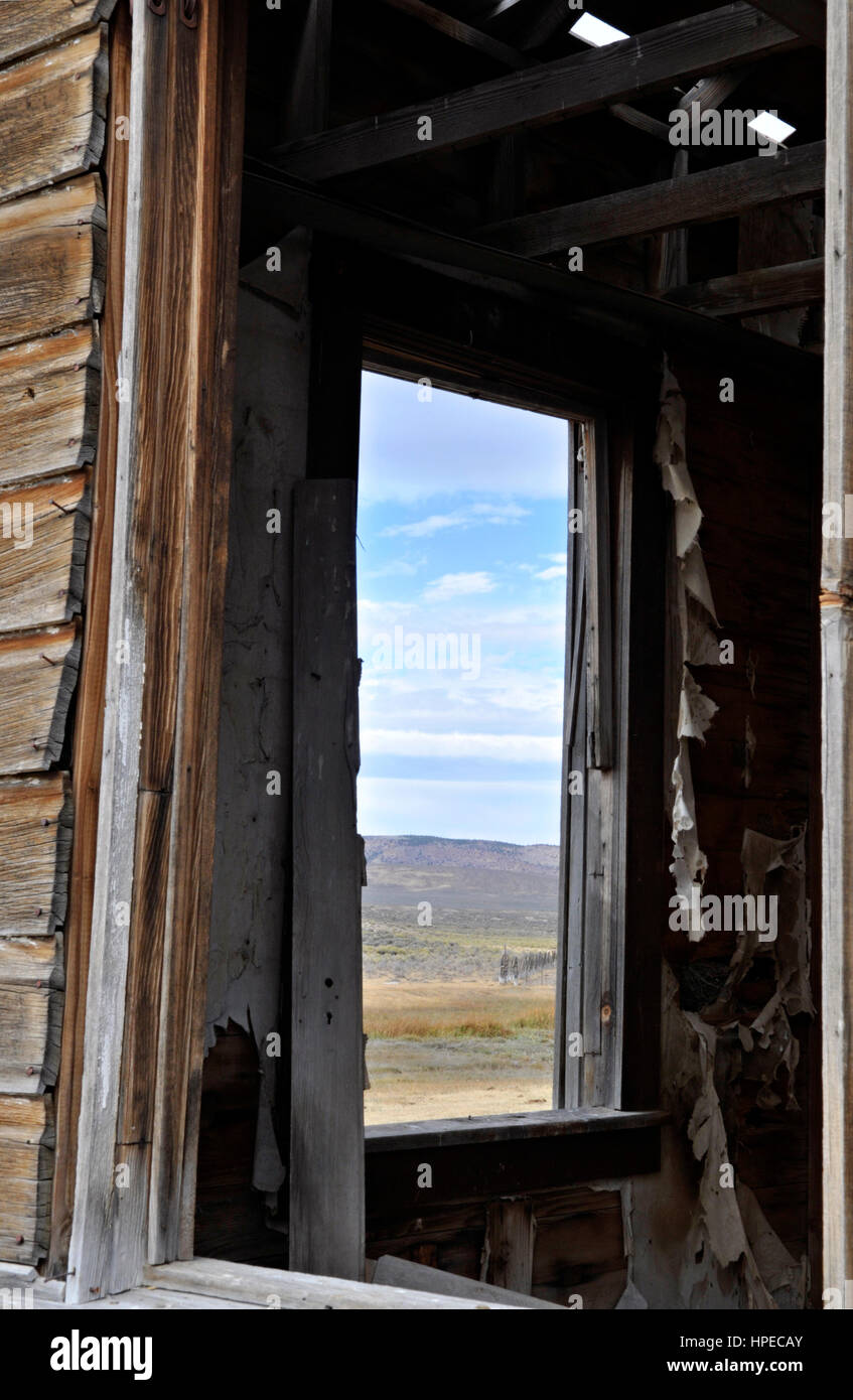 En regardant par la fenêtre d'un bâtiment abandonné en décomposition dans un ranch à un paysage désertique, montagneux. Banque D'Images
