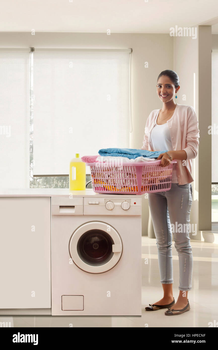 Jeune femme debout près de lave-linge panier à linge holding Banque D'Images Jeune femme debout près de lave-linge panier à linge holding Banque D'Images