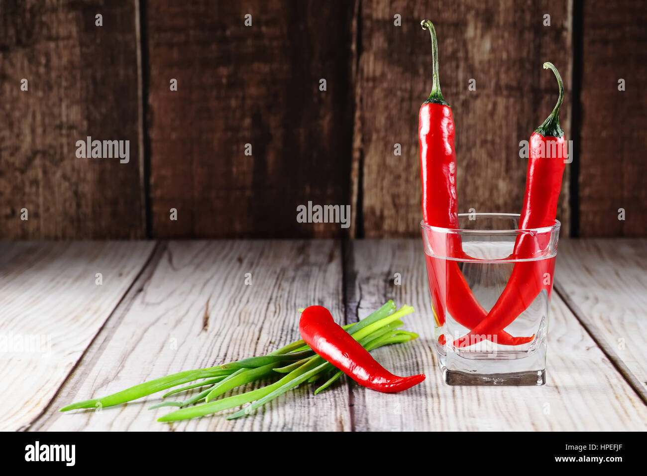 Red Hot Chili Peppers et les oignons verts dans verre d'eau sur fond de bois Banque D'Images