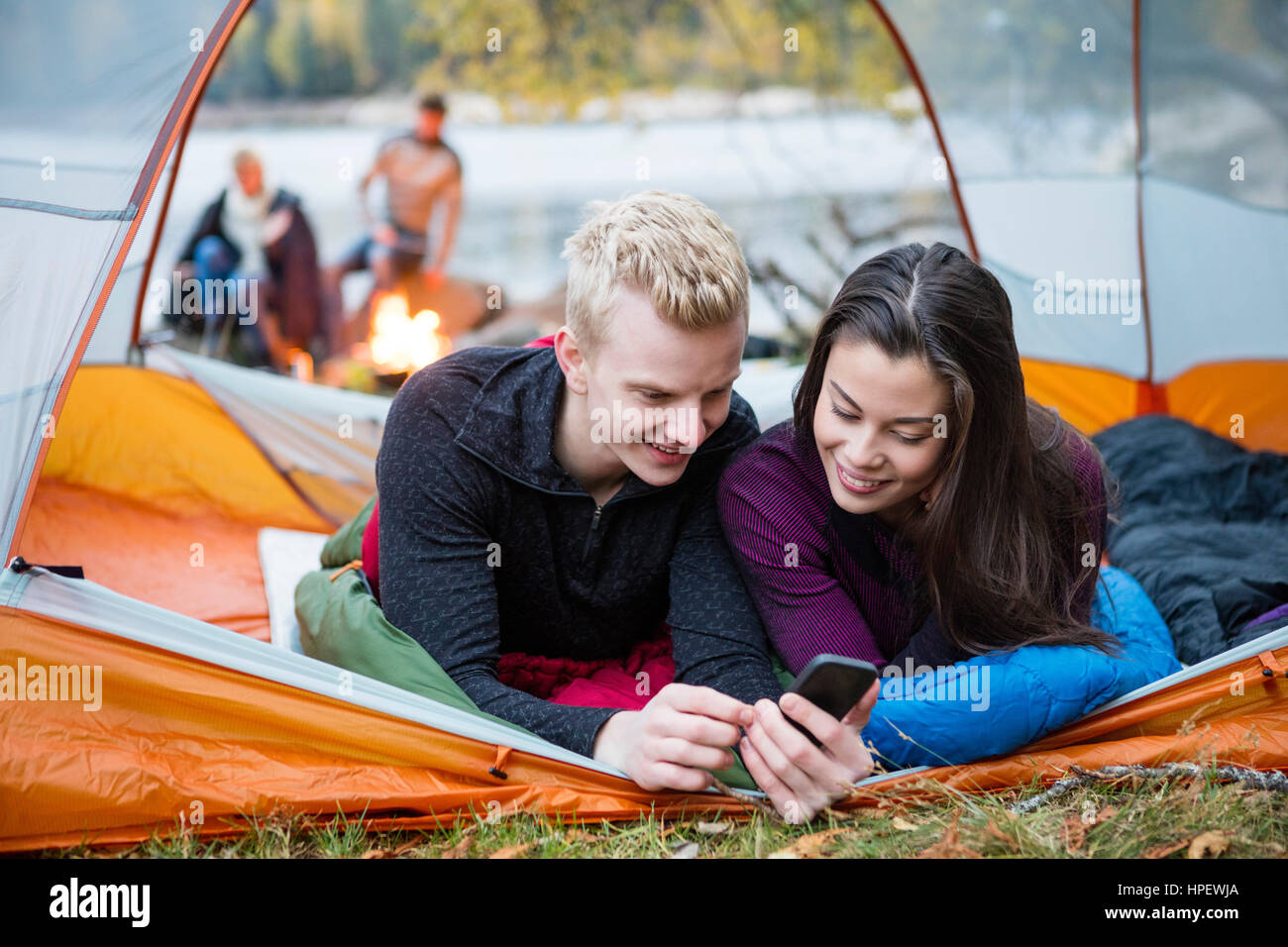 Jeune couple à l'aide de téléphone mobile en tente sur le camping au bord du lac Banque D'Images