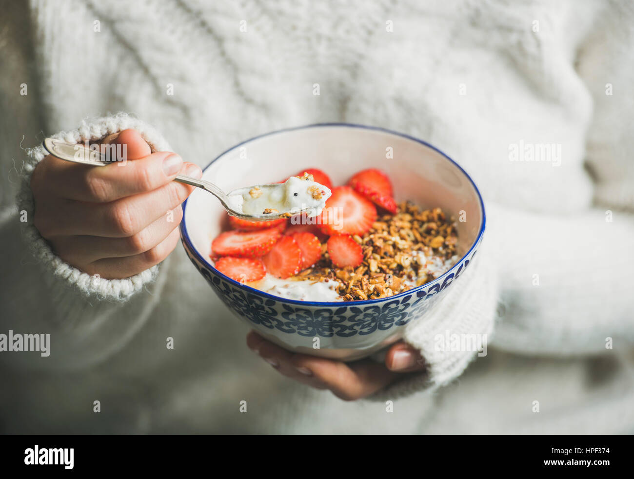 Petit-déjeuner sain du yaourt grec, granola et bol de fraises dans les mains de woman wearing white loose pull en laine tricotée, selective focus. Eatin'Mpropre Banque D'Images