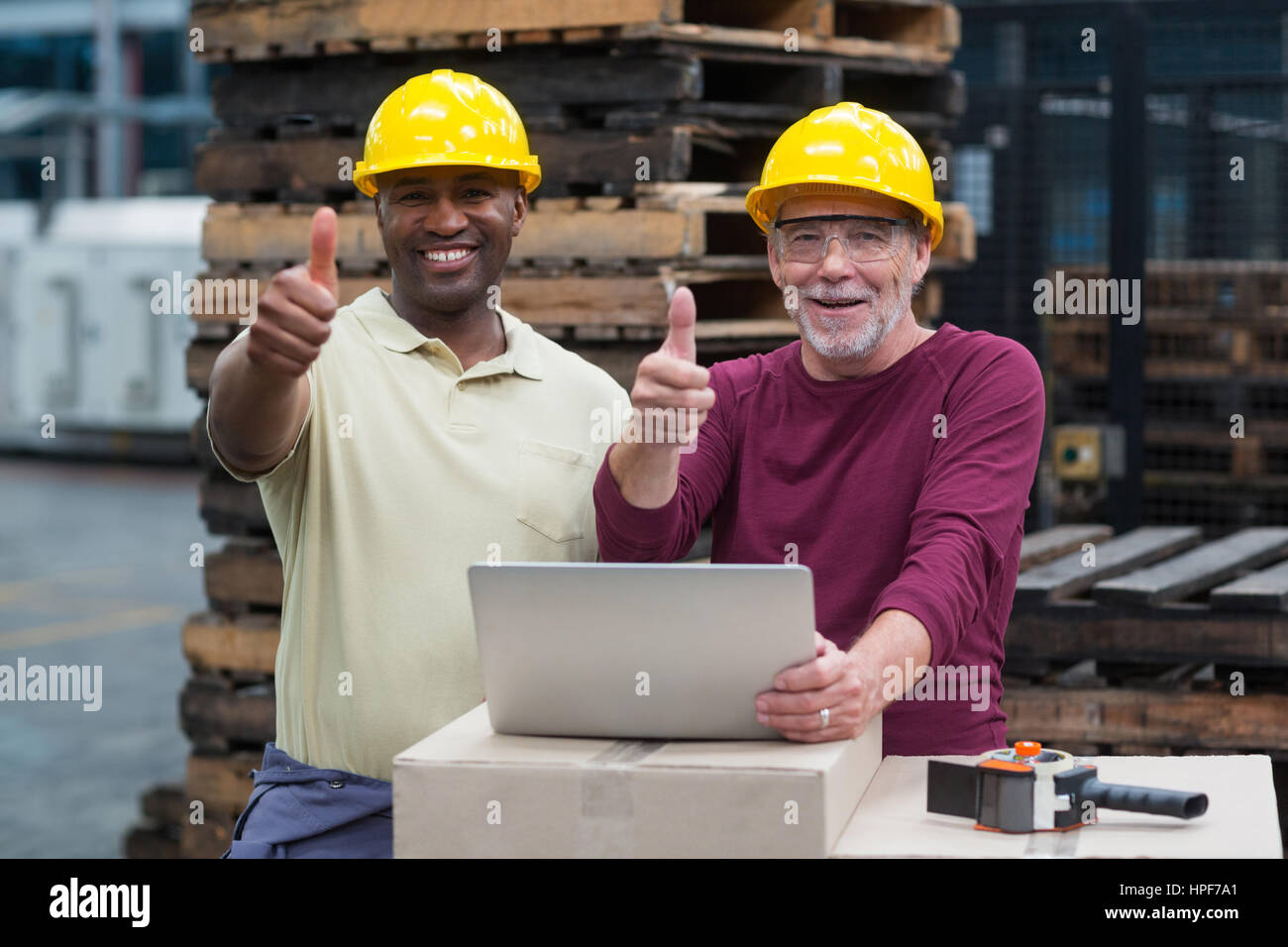Portrait de deux travailleurs d'usine avec ordinateur portable montrant les pouces jusqu'à l'usine de production de boissons Banque D'Images