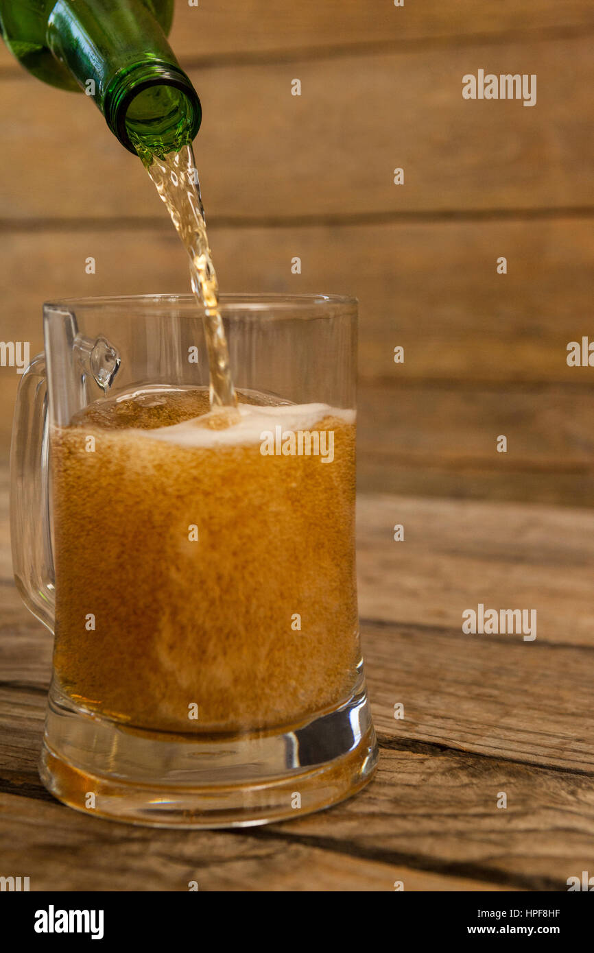 La bière est versé dans un mug contre fond de bois Banque D'Images