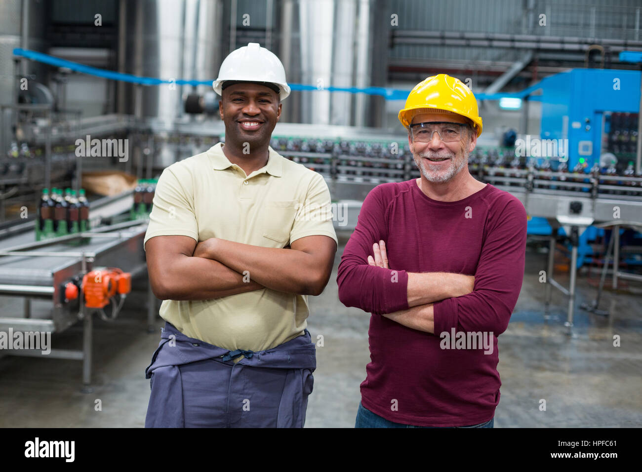 Portrait de deux ouvriers debout avec leurs bras croisés dans l'usine de production de boissons Banque D'Images