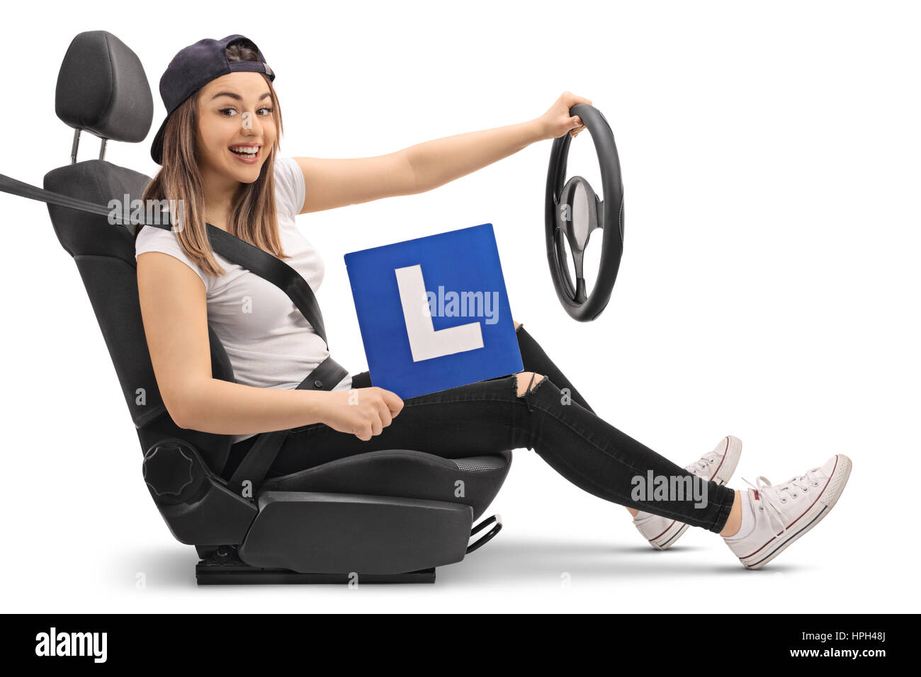 Happy girl holding an L-signer et faire semblant de conduire dans un siège de voiture isolé sur fond blanc Banque D'Images