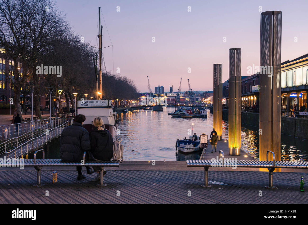 Un couple s'asseoir dehors sur un banc avec vue sur le port de Bristol juste après le coucher du soleil en début de soirée et profiter de la vue. Banque D'Images