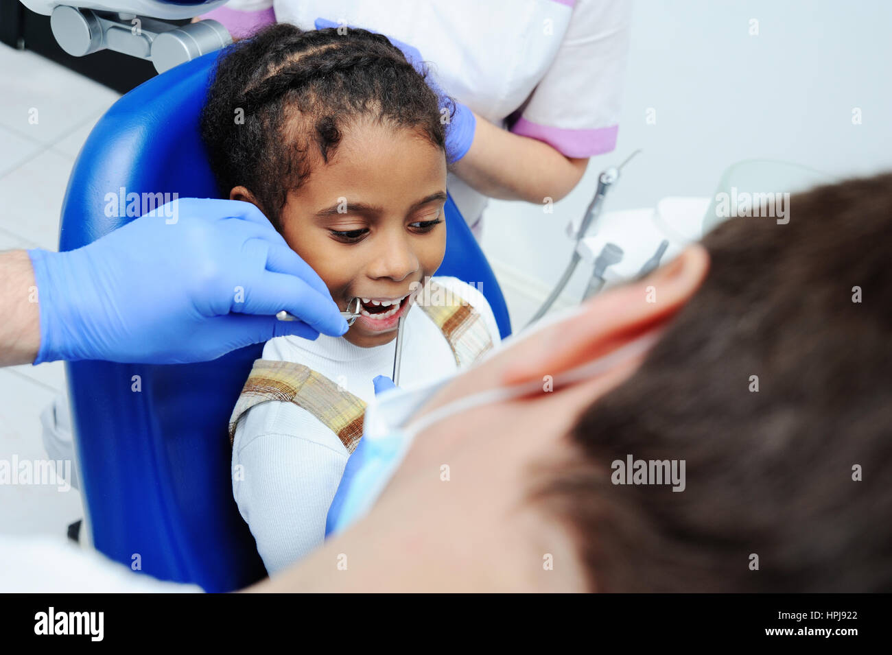 Peu ethnique afro-américaine black female smiling while dentiste dans des  gants en latex blanc contrôle de l'état de ses dents. bébé fille en bleu  fauteuil dentaire Photo Stock - Alamy