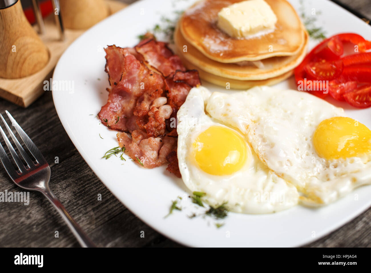 Délicieux petit-déjeuner avec des œufs, des pancakes, du bacon et des légumes. Banque D'Images