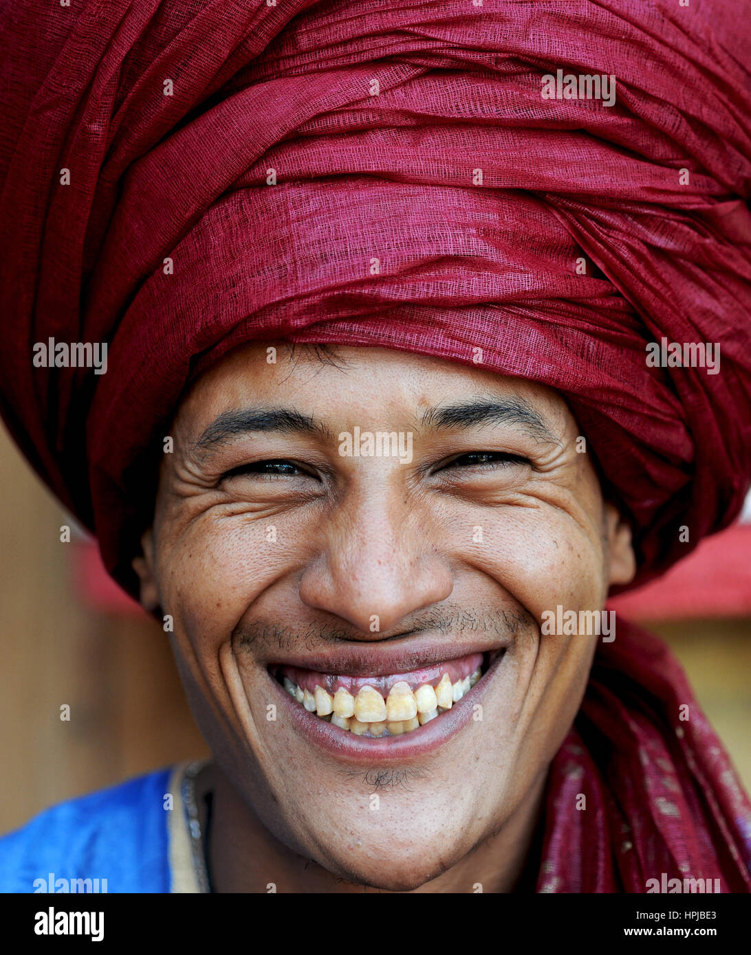 Portrait d'un Bédouin nomad avec turban écarlate et grand sourire de vendre ses marchandises dans populaires site du patrimoine mondial de Ait Benhaddou au Maroc. Banque D'Images