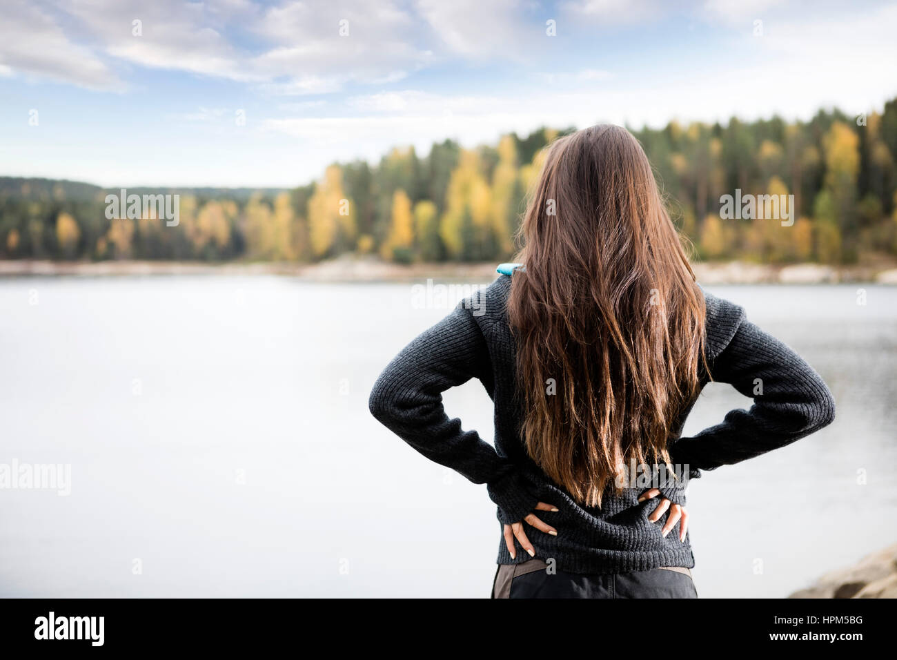 Vue arrière du jeune femme debout avec les mains sur les hanches, par lac au cours de l'automne Banque D'Images