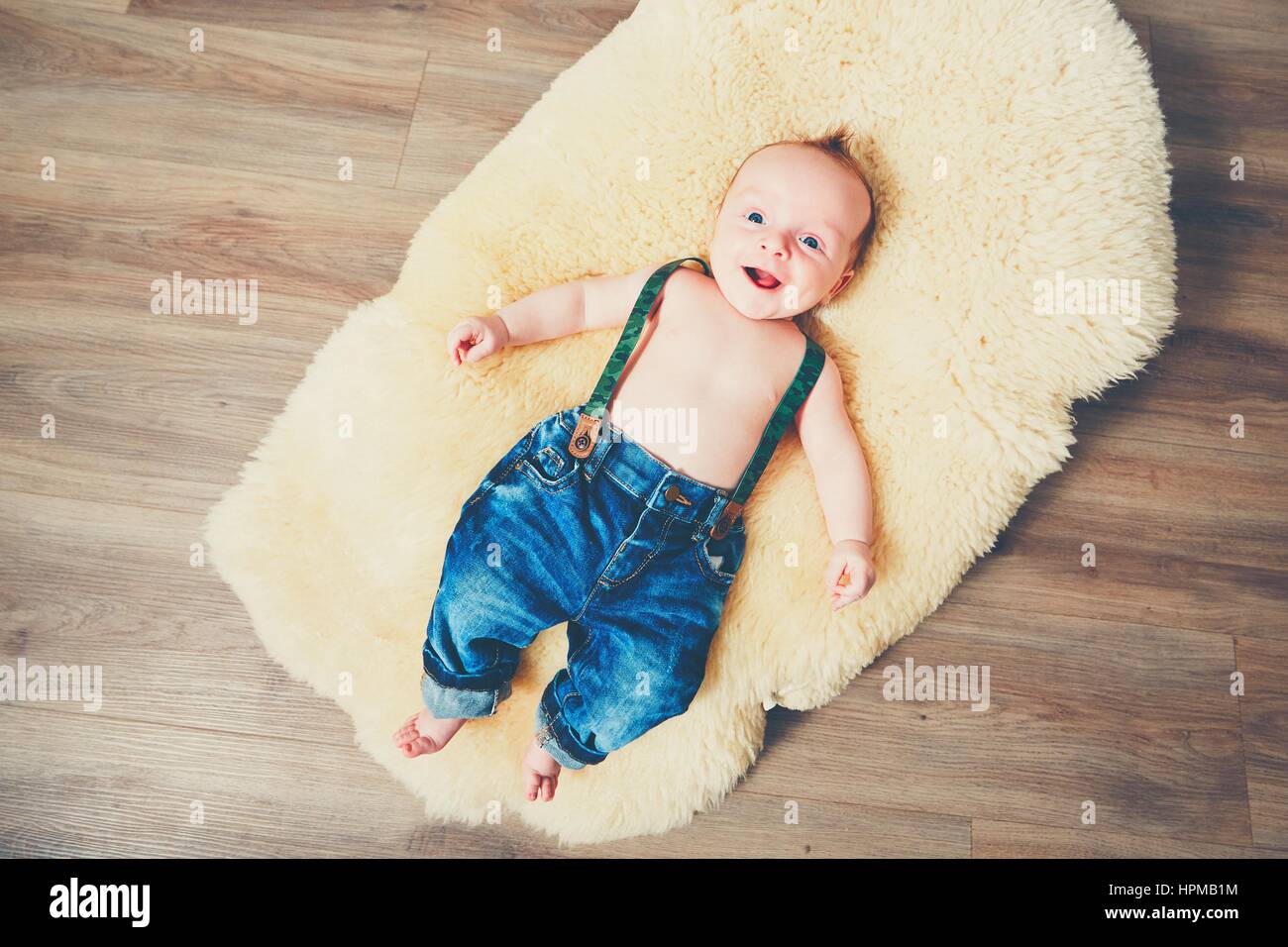 Petit garçon à la maison. Adorable bébé reposant sur la couverture de fourrure en bois sur l'étage. Banque D'Images