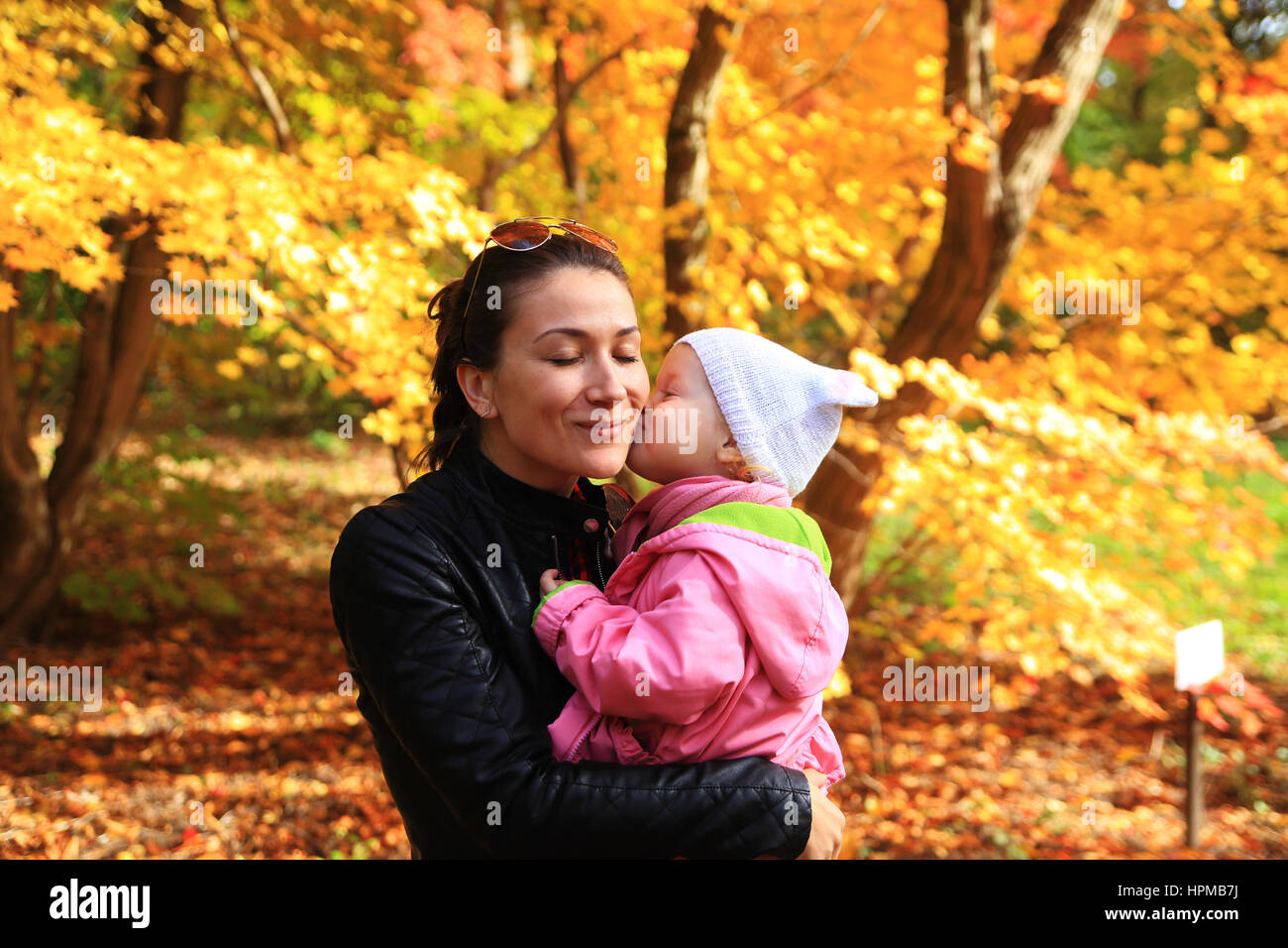 Little girl kissing her mom sur automne fond Banque D'Images