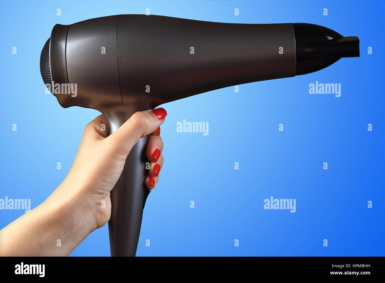 Sèche-cheveux dans la main des femmes. Fond bleu. La main avec des clous rouges. Banque D'Images