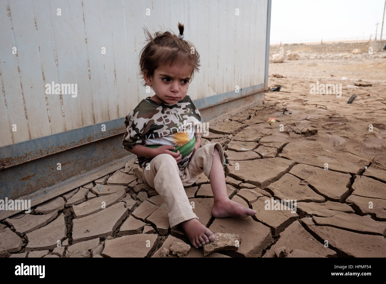 Une jeune fille est assise sur la fissure sèche terre en dehors de l'école au pied de la face nord de Sinjar Mountain près de la ville d'Snuny, Iraq Banque D'Images