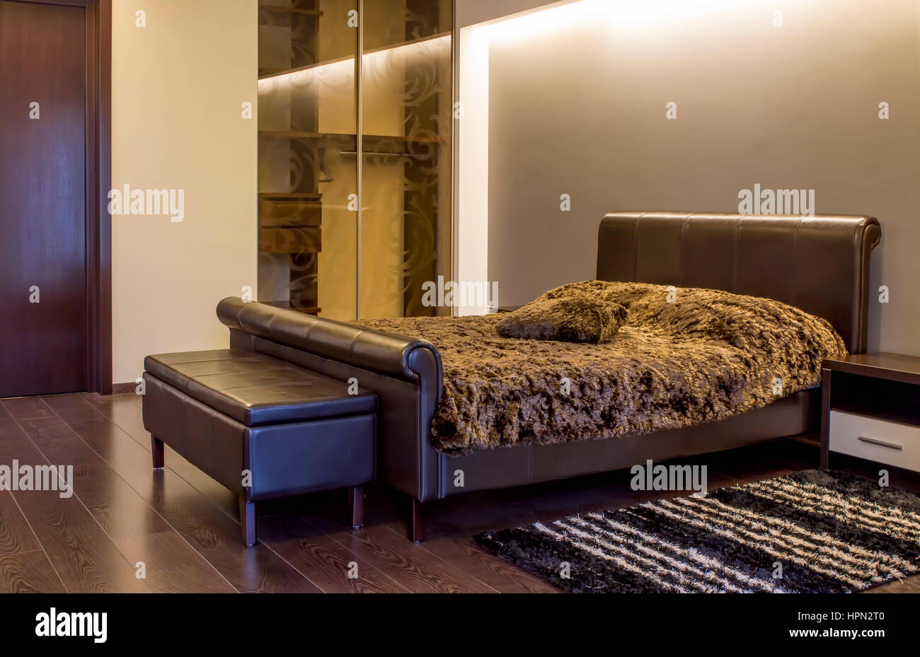 Intérieur chambre à coucher moderne avec l'éclairage ambiant et d'un élégant lit en face d'un mur blanc dans une maison luxueuse. Banque D'Images