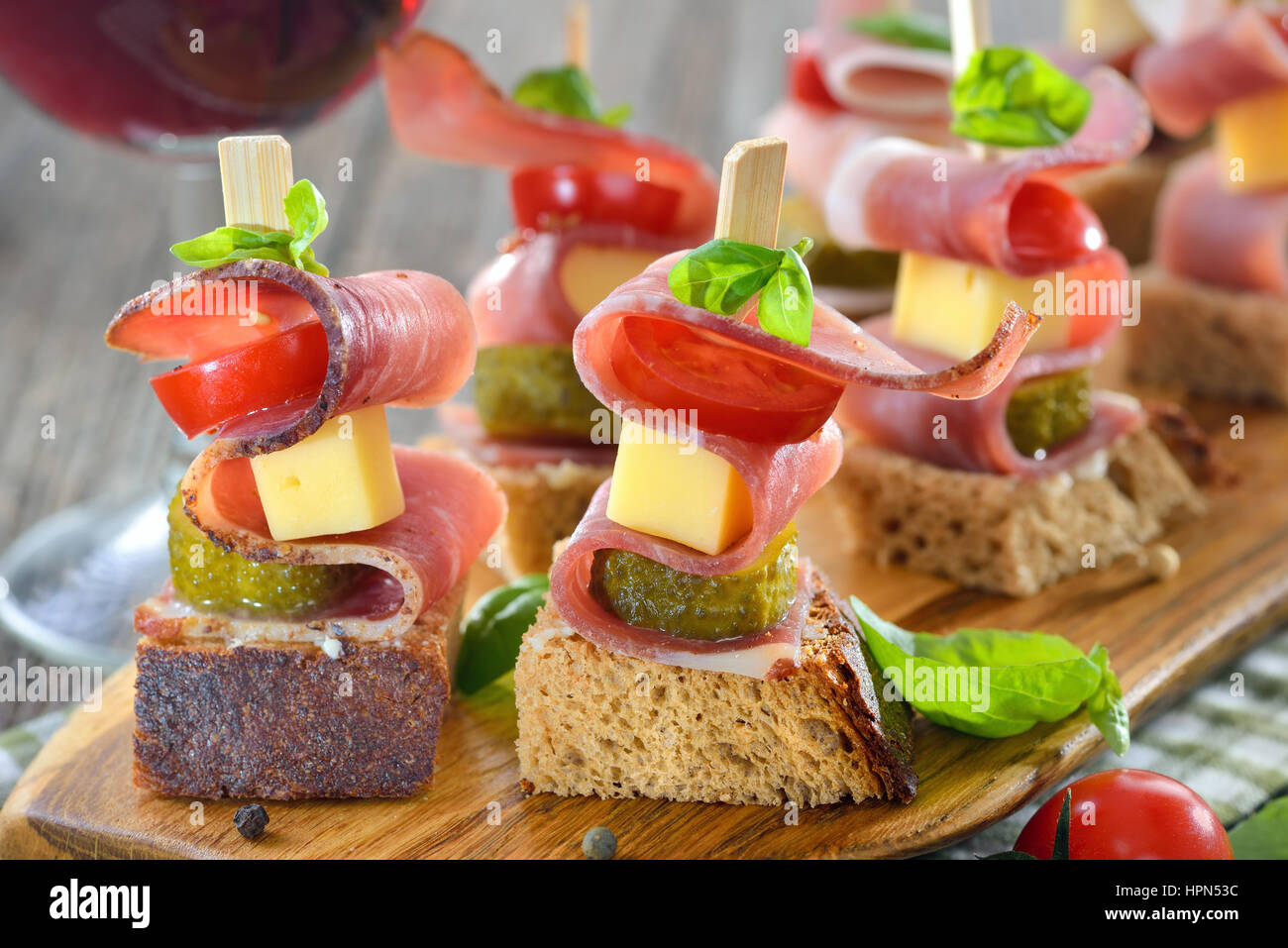 Apéritifs du Tyrol du Sud : pain de campagne frais beurré avec le lard fumé, fromage de montagne copieux, les cornichons et les tomates, les feuilles de basilic sur le dessus Banque D'Images Apéritifs du Tyrol du Sud : pain de campagne frais beurré avec le lard fumé, fromage de montagne copieux, les cornichons et les tomates, les feuilles de basilic sur le dessus Banque D'Images