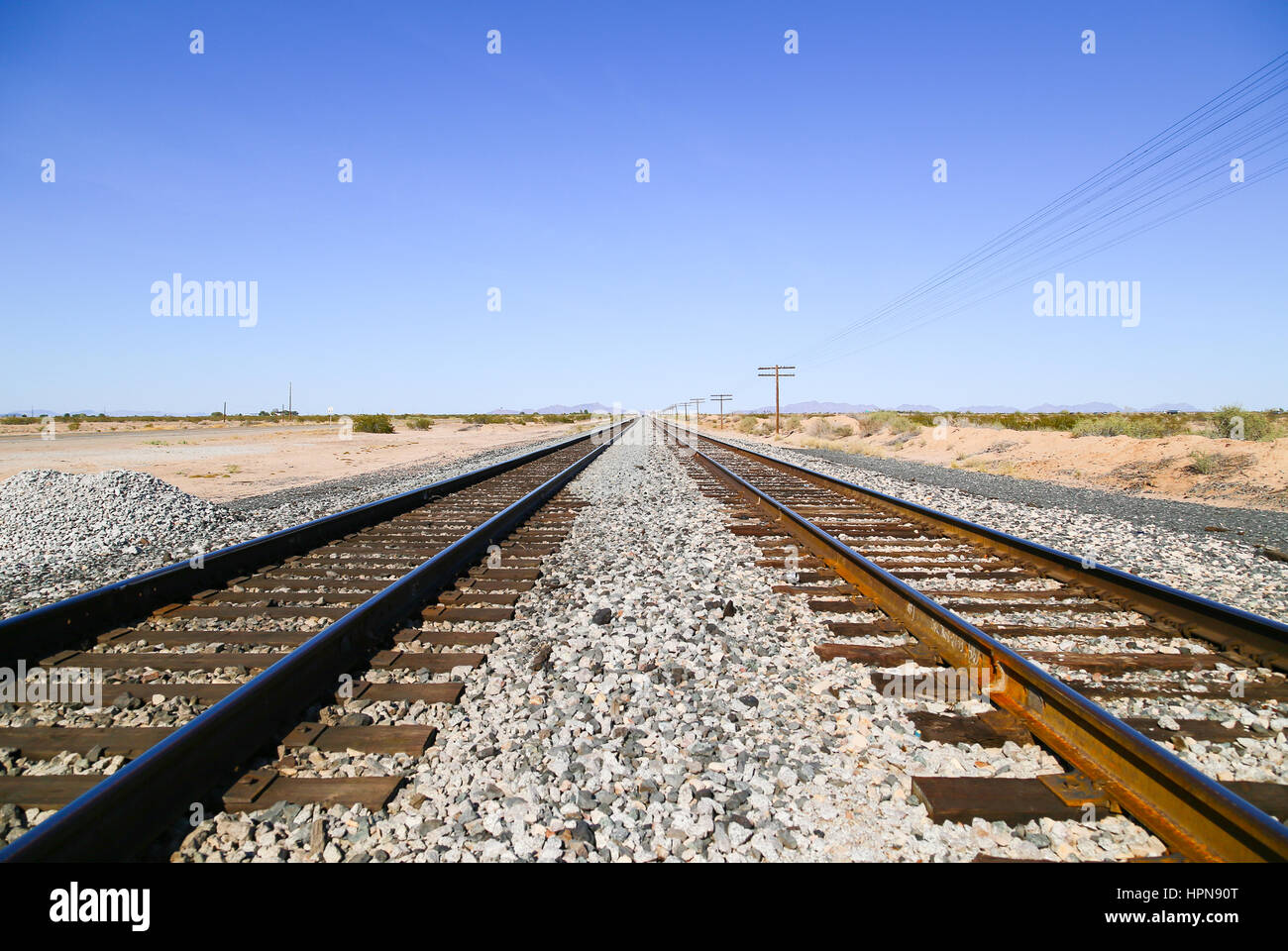 Des voies de chemin de fer dans le désert de Sonora, en Arizona, USA, avec des câbles électriques aériens d'un côté et de l'ancien US Highway 80 à l'autre et d'un rang de montagne Banque D'Images