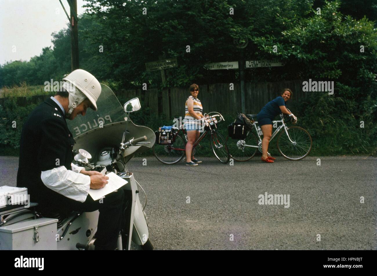 Un agent de police moto écrit sur un morceau de papier tandis que deux cyclistes regardez sur, près de West Tytherley, Hampshire, United Kingdom, 1970. Banque D'Images