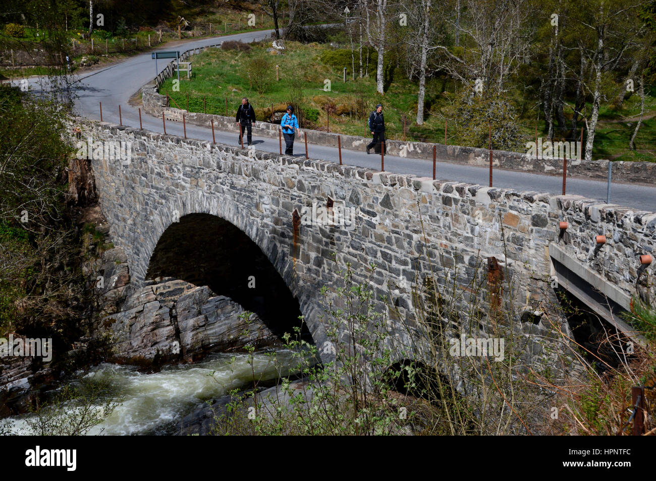 Trois marcheurs traversant le pont du chemin de pierre sur la rivière Feshie Feshiebridge ay sur l'East Highland Way dans les Highlands, Ecosse, Royaume-Uni. Banque D'Images