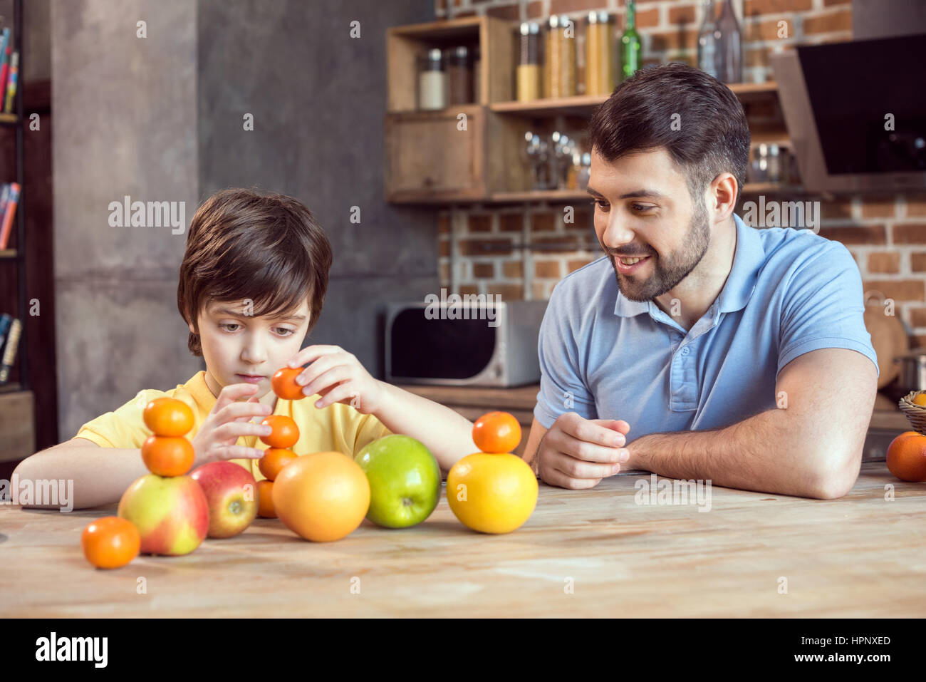 Père et fils jouant avec les agrumes à table de cuisine Banque D'Images