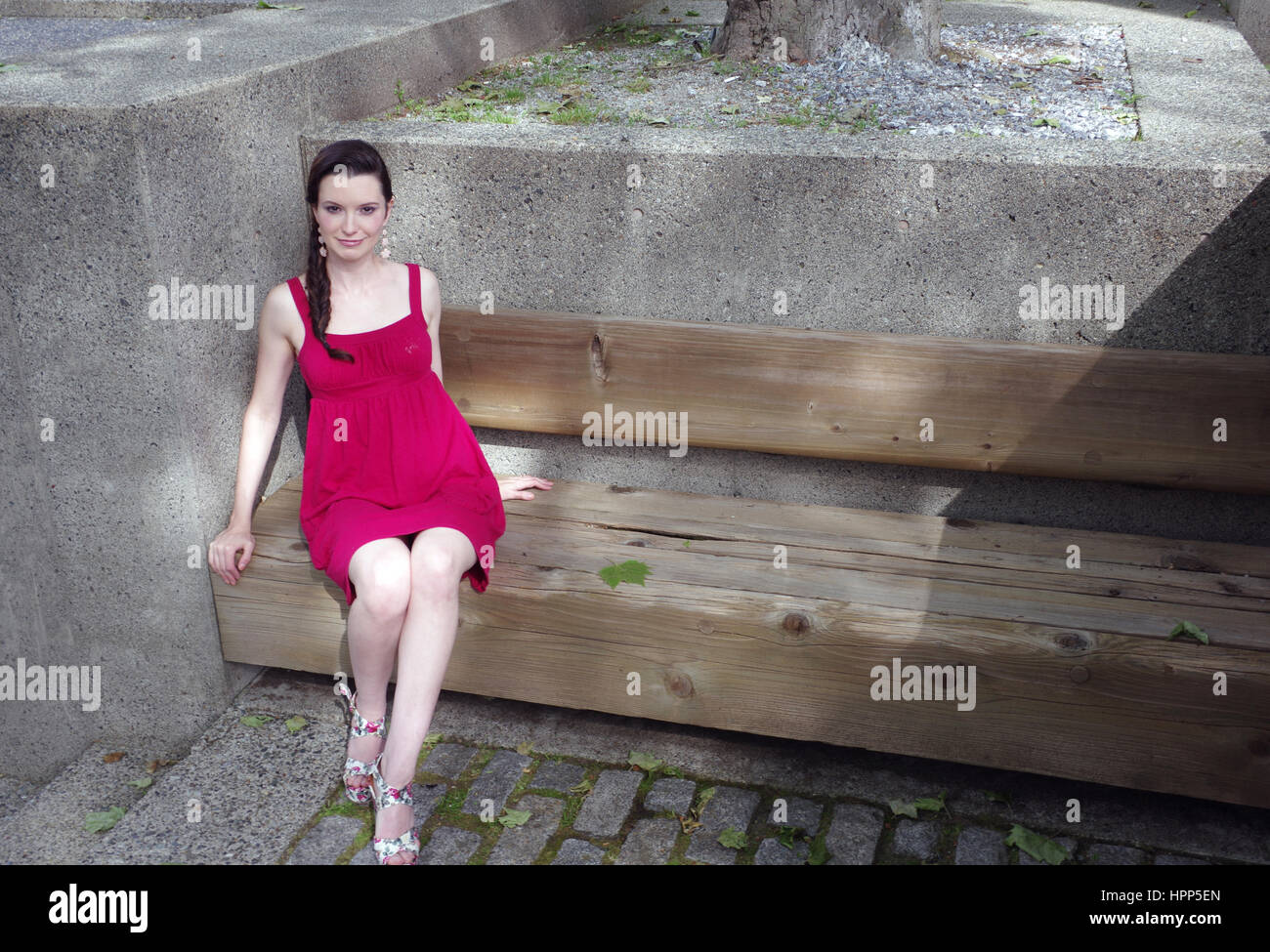 Woman wearing red dress allongé sur un banc au soleil dans la ville Banque D'Images