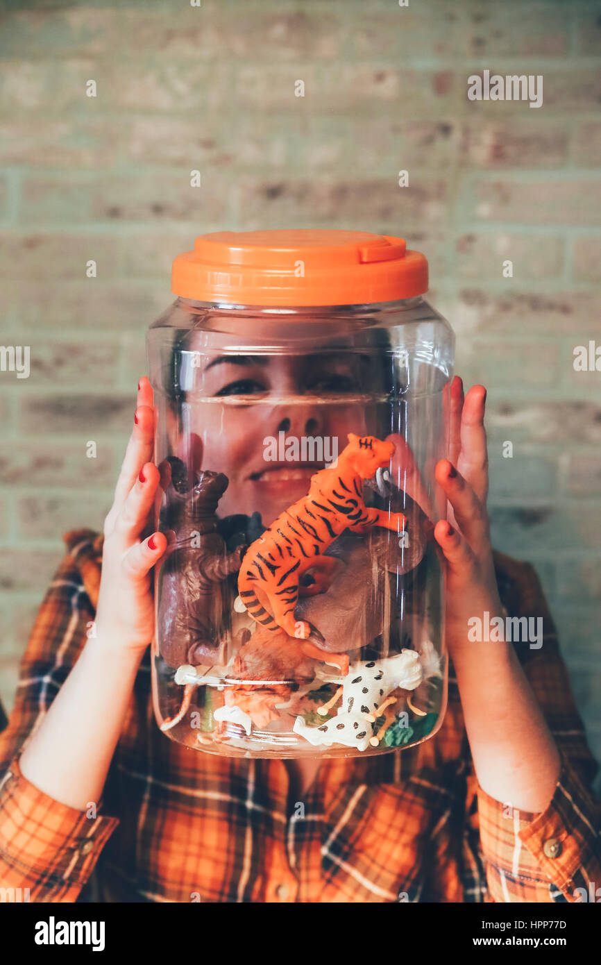 Femme drôle appuyant sur son visage contre le pot avec des animaux en plastique Banque D'Images