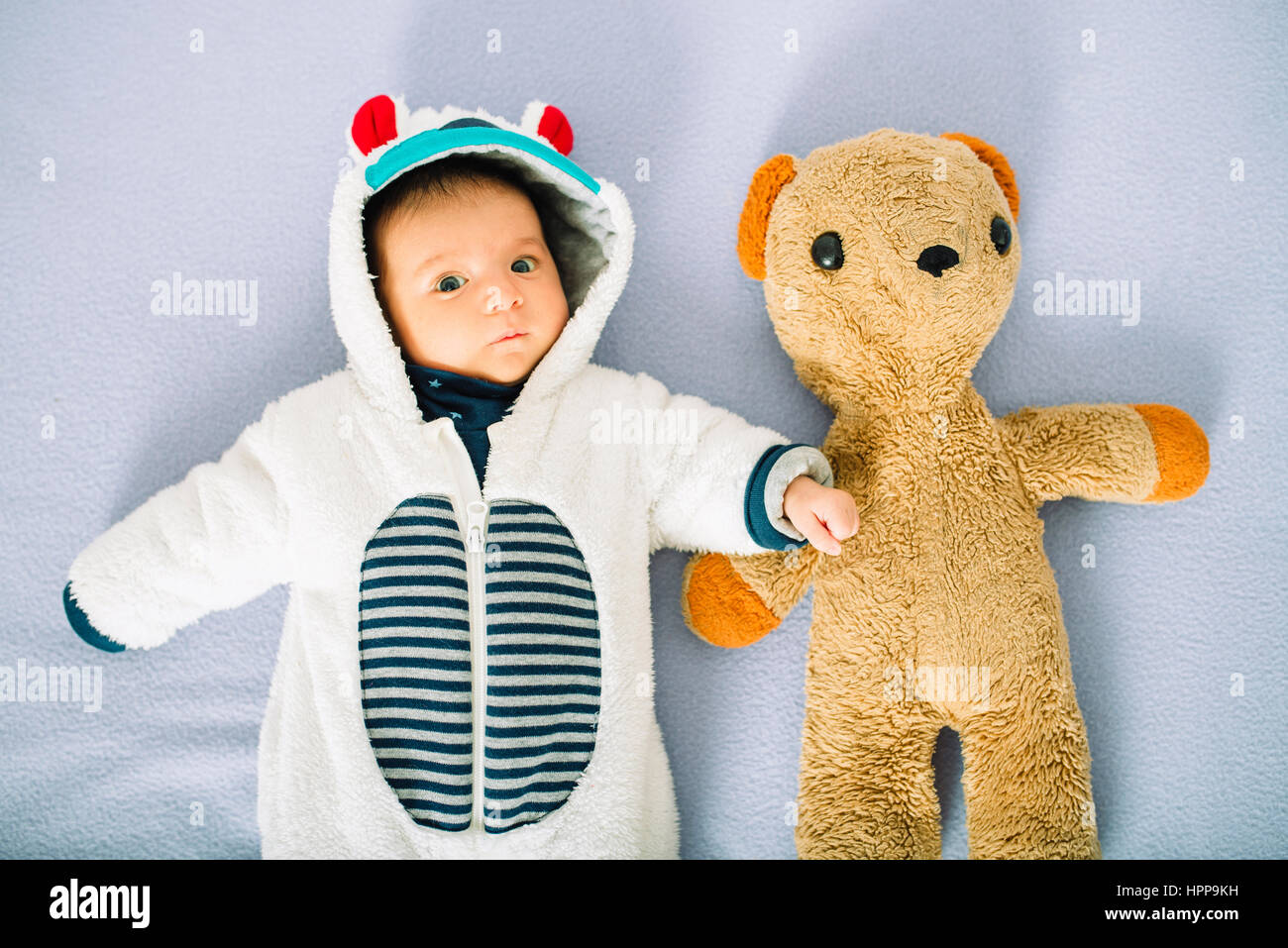 Naissance bebe Fille sur lit vêtu d'un costume d'ours à côté d'un ours en peluche Banque D'Images