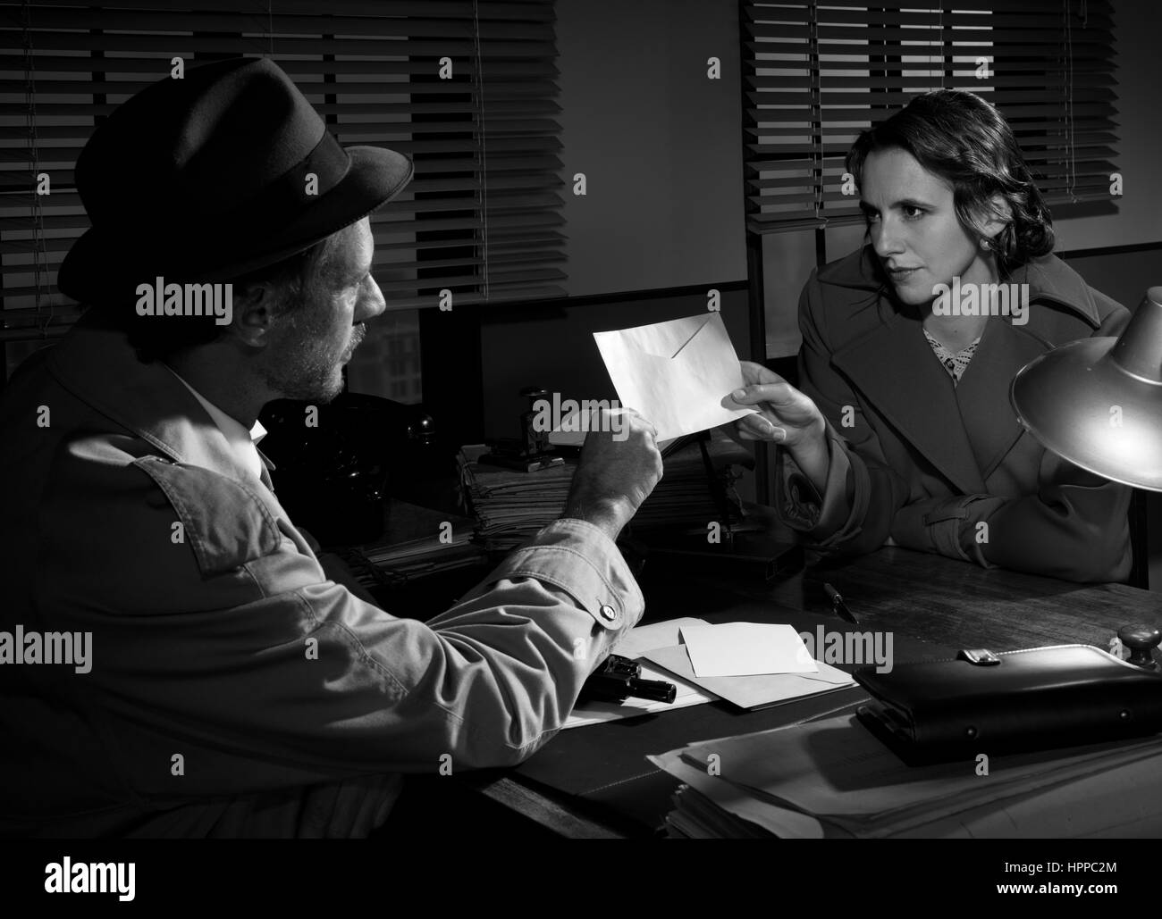 Femme remettant une enveloppe d'un détective au poste de police, 1950 film noir style. Banque D'Images