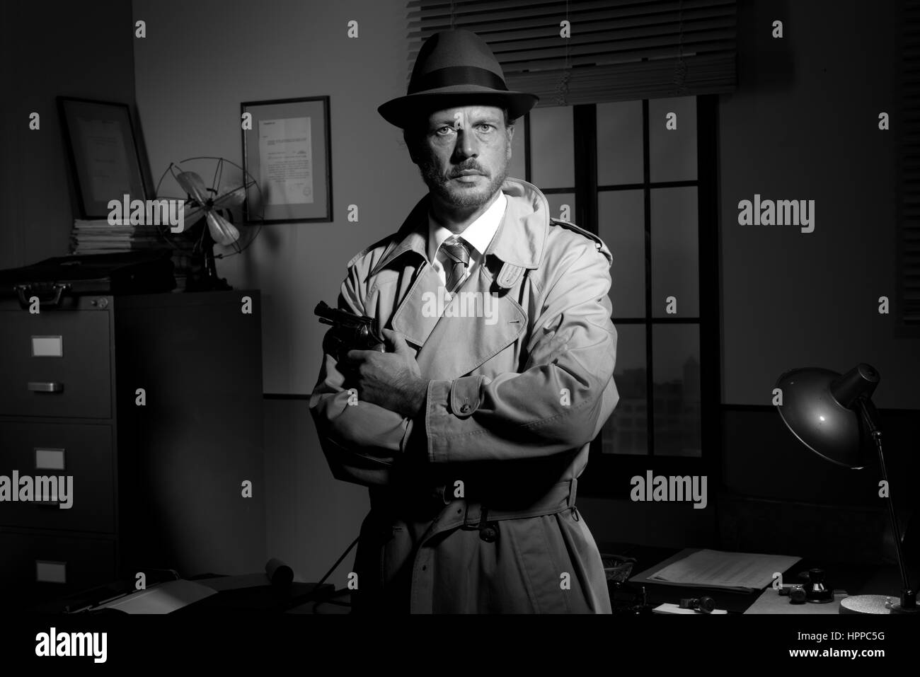 Détective attrayant tenant un revolver à bureau rétro sur arrière-plan, le film noir. Banque D'Images