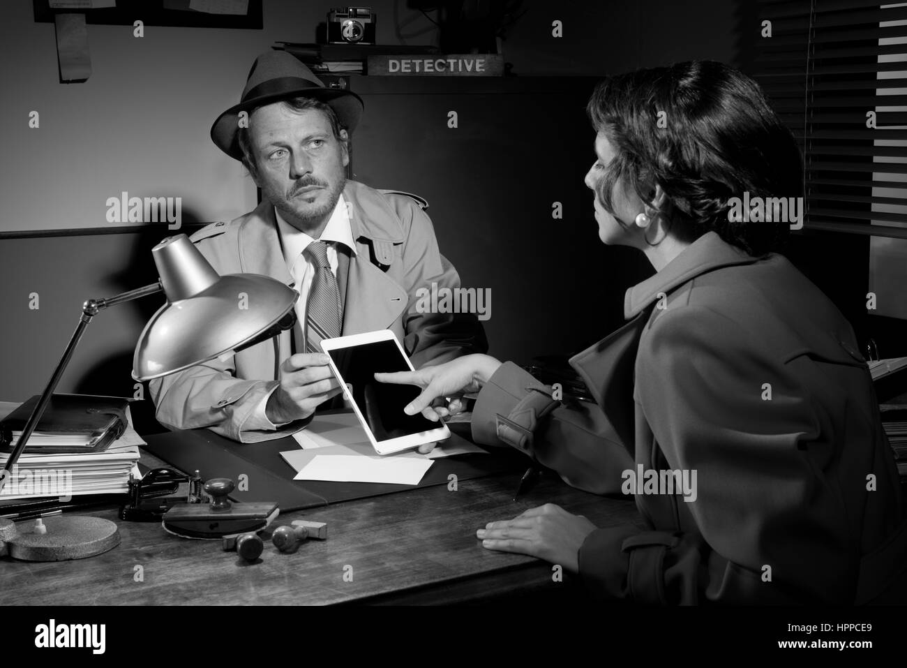 Woman touching tablet du détective assis à son bureau. Banque D'Images
