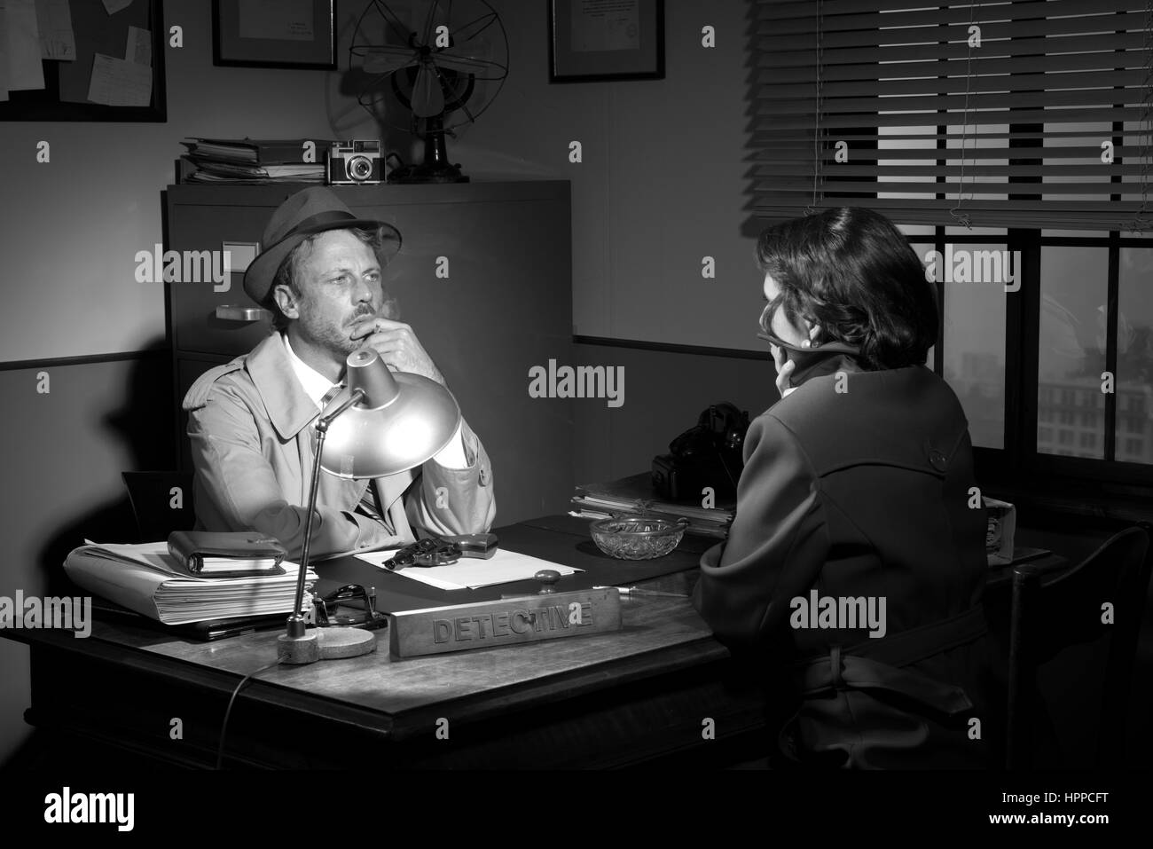 Beau bureau de détective bureau interrogeant une jeune femme, 1950 film noir style. Banque D'Images