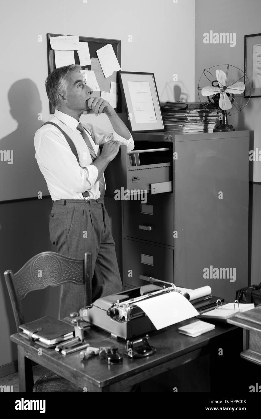 Pensive office worker à la recherche d'un fichier dans un cabinet vintage with hand on chin. Banque D'Images