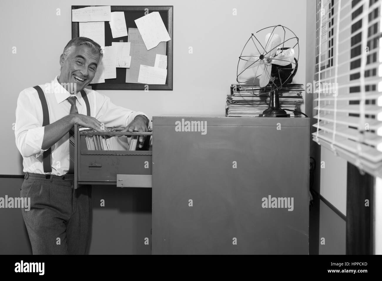 Cheerful smiling employé dans les années 1950, le bureau de style la recherche d'un fichier dans l'armoire. Banque D'Images