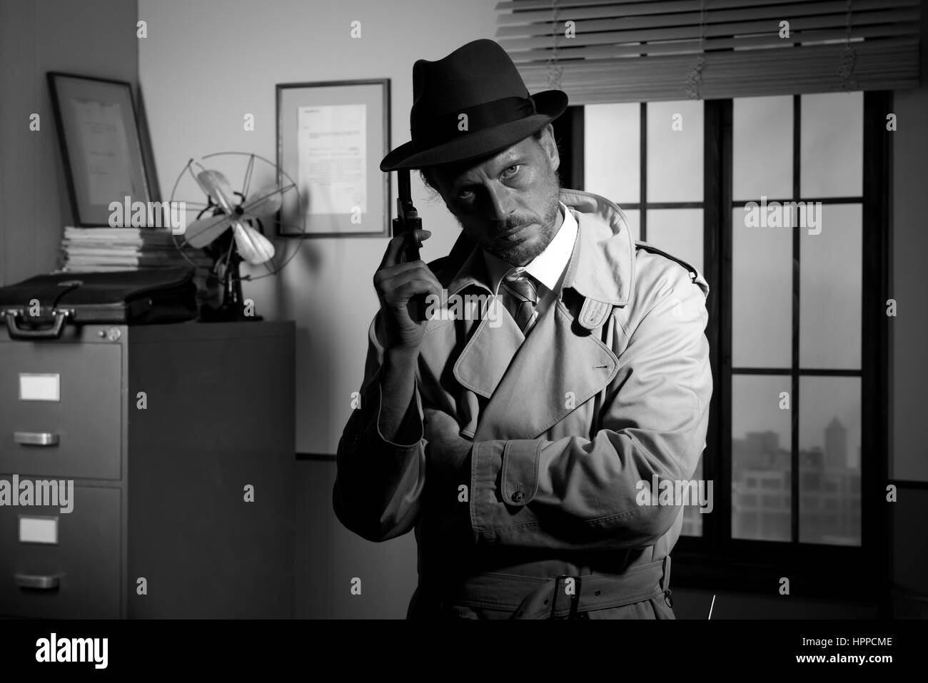 Détective attrayant tenant un revolver à bureau rétro sur arrière-plan, le film noir. Banque D'Images